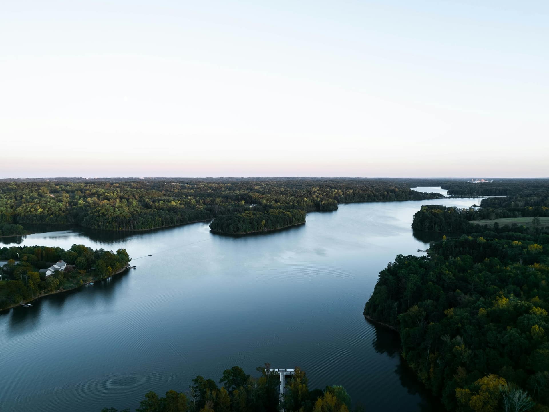 Aerial view of a wide, tree-lined lake with wooded shores and a few lakeside homes